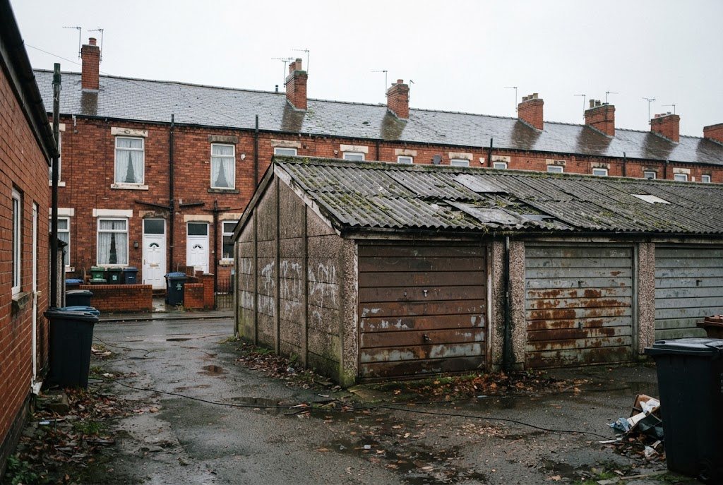 Old concrete sectional garage with a weathered asbestos cement roof behind red-brick terraced houses
